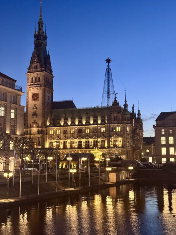 Das Hamburger Rathaus am Abend mit Lichtern die sich im Wasser spiegeln