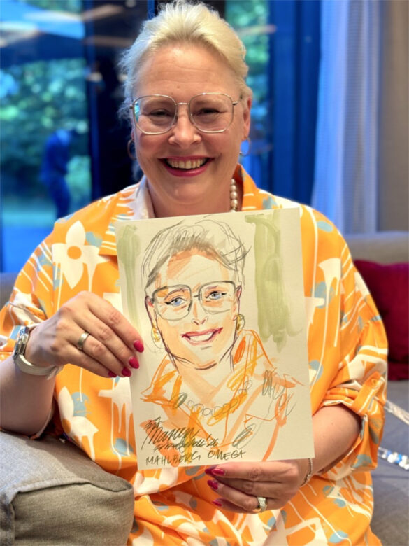 Eine Teilnehmerin der Juwelier Mahlberg + Omega Veranstaltung zeigt ihr handgezeichnetes Portrait, das Felix Scholz während des Events im Hotel Kieler Kaufmann als Live-Illustration angefertigt hat.