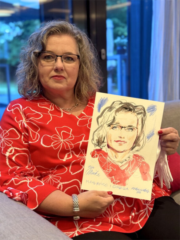Eine Teilnehmerin der Juwelier Mahlberg + Omega Veranstaltung zeigt ihr handgezeichnetes Portrait, das Felix Scholz während des Events im Hotel Kieler Kaufmann als Live-Illustration angefertigt hat.