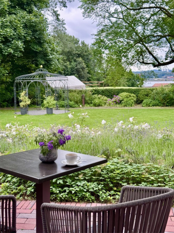 Der Parkartige Garten des Hotels Kieler Kaufmann mit Kaffeetisch, einem Pavillion und dem Blick auf die Kieler Förde
