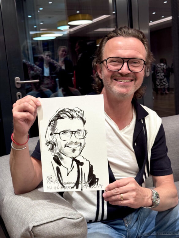 Gast der Veranstaltung von Juwelier Mahlberg und Omega im Hotel Kieler Kaufmann zeigt eine persönliche Portraitzeichnung von Felix Scholz, entstanden als Live-Illustration während des Events.